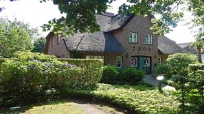 Ein traditionelles Backsteinhaus mit einem Reetdach, umgeben von gepflegten Hecken und blühenden Pflanzen.