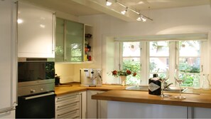Eine moderne Küche mit weißen Schränken, einem eingebauten Ofen, einer Kaffeemaschine und einem Fenster mit Blick ins Grüne.