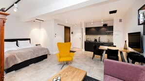 Un appartement moderne comprenant un lit, un fauteuil jaune, une table à manger et un coin cuisine.