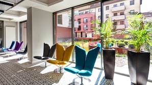 Un espace d’attente moderne, doté de chaises colorées et de grandes fenêtres donnant sur un immeuble d’habitation.