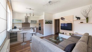 Una sala moderna con un sofá, una mesa de centro de vidrio y un televisor. Cuenta con una zona de cocina con una barra y una mesa de comedor.