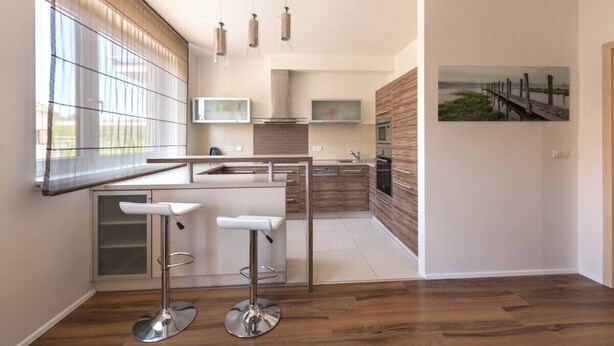 Una cocina moderna con un ventanal grande, una isla de madera con taburetes de bar y un cuadro en la pared.