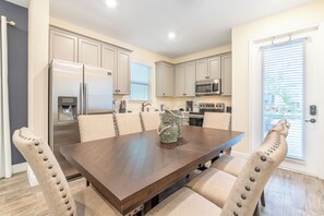 A modern kitchen with white cabinets, stainless steel appliances, and a dining area with a wooden table and cushioned chairs.