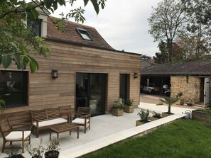 A modern house with a patio area featuring wooden furniture and potted plants. - Charming and comfortable renovated house in Pays de la Loire (Durtal)