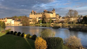Un edificio histórico con un foso, rodeado de jardines bien cuidados y un río.