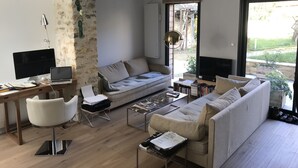 Uma sala de estar moderna com um sofá grande, uma escrivaninha com um computador e uma estante de livros.