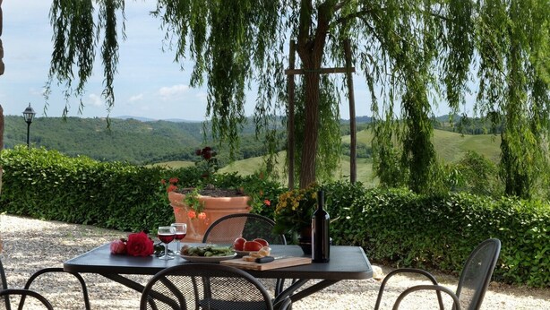 An outdoor dining area with a table set for two, surrounded by greenery and overlooking a scenic landscape. - San Lorenzo Agriturismo (Buonconvento)