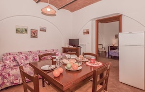 A dining area with a wooden table set for two, a sofa with a floral pattern, and a television in the background.