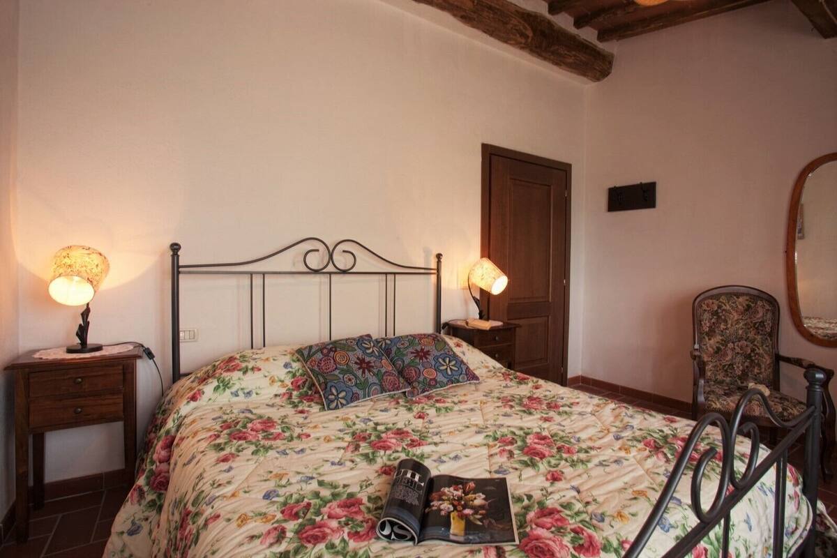 Un dormitorio con colcha estampada, dos lámparas de noche, una puerta de madera, una silla y un espejo en la pared.