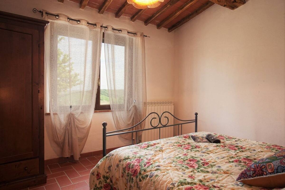 Un dormitorio con cama, cortinas, radiador y armario de madera.