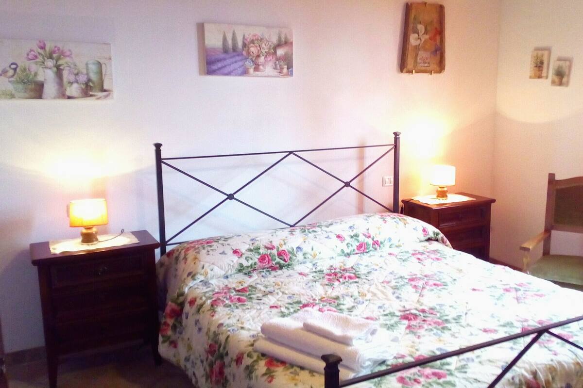 Un dormitorio con una cama, dos mesitas de noche con lámparas, una silla y decoración en la pared.