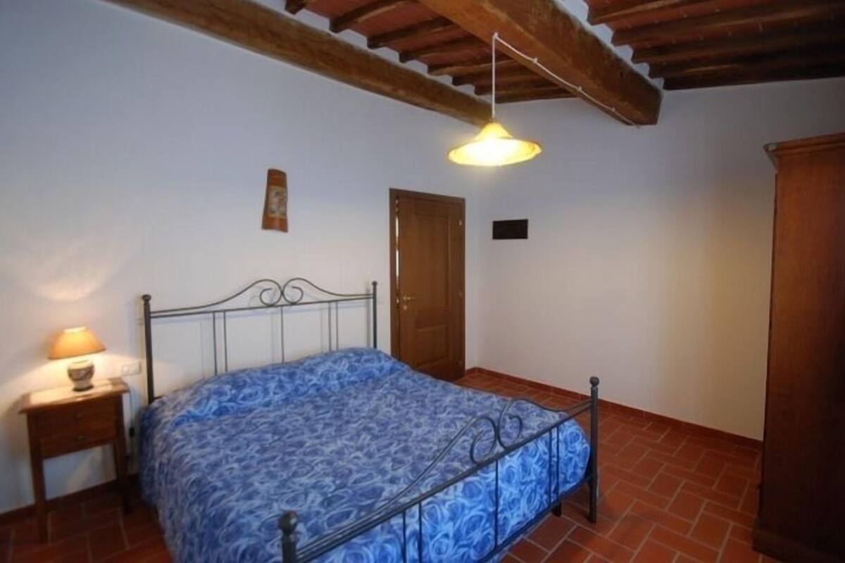 Un dormitorio con cama, mesita de noche, puerta de madera y ventilador de techo.
