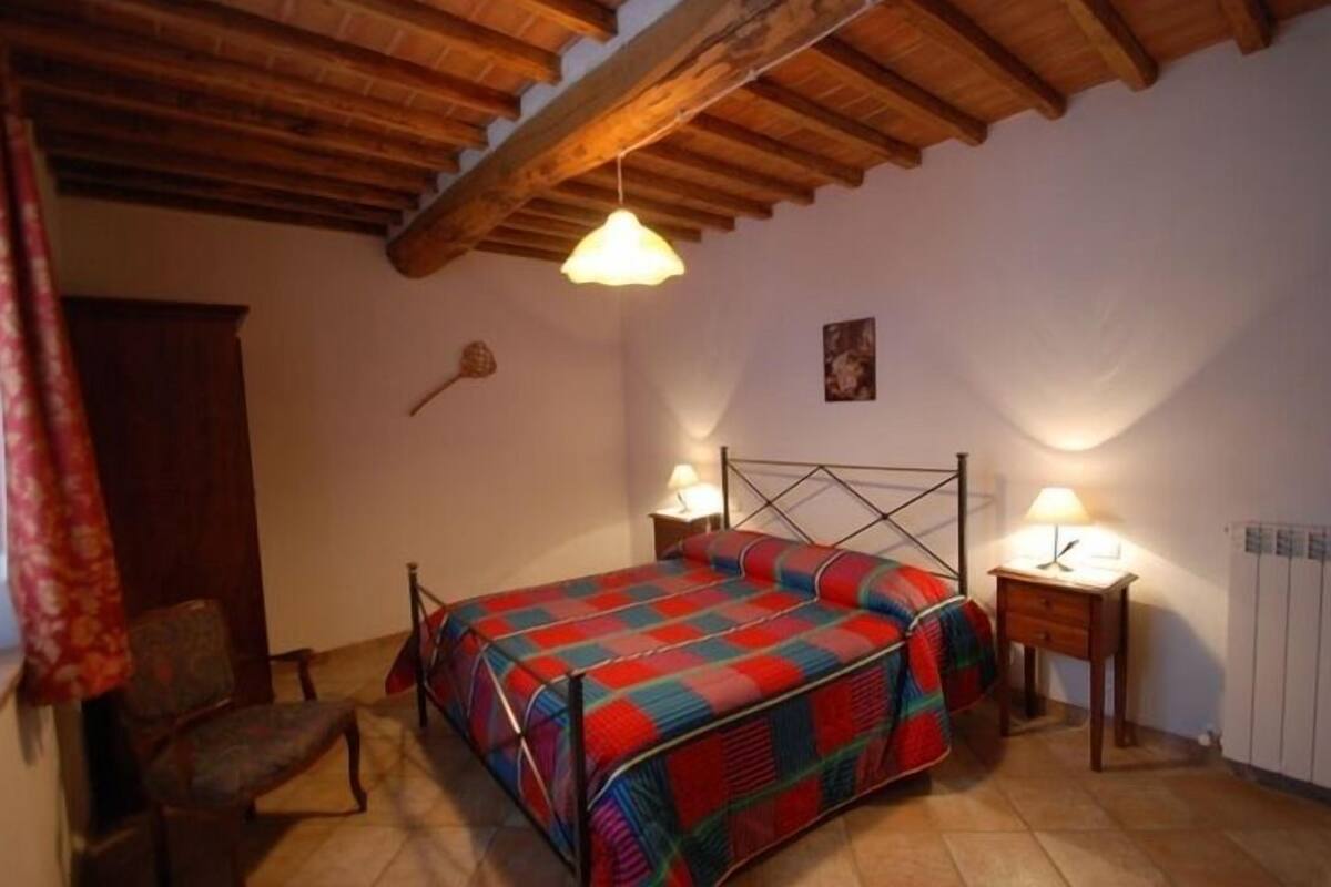Un dormitorio con cama, dos mesitas de noche, una silla y techo de madera.