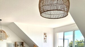 A dining area with a white table and chairs, a woven light fixture, and a view of the outdoors through large windows. - Magnificent apartment - Beautiful sea view - Wifi included (Quiberon)