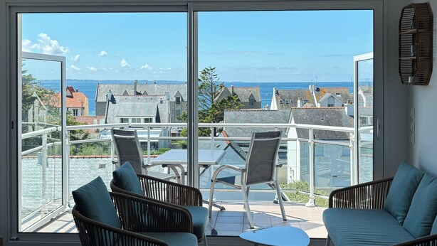A balcony with wicker furniture, a glass table, and a view of the sea and buildings. - Magnificent apartment - Beautiful sea view - Wifi included (Quiberon)