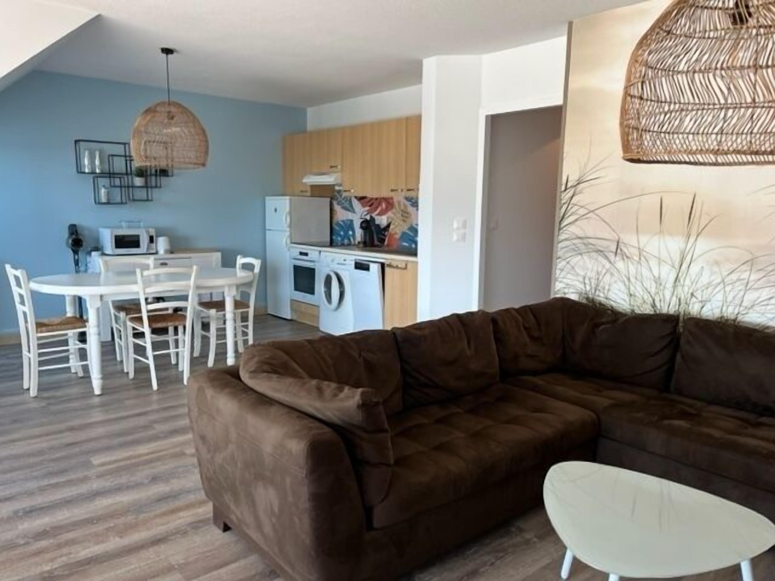 A modern living room with a brown sofa, a white coffee table, and a dining area with a white table and chairs.