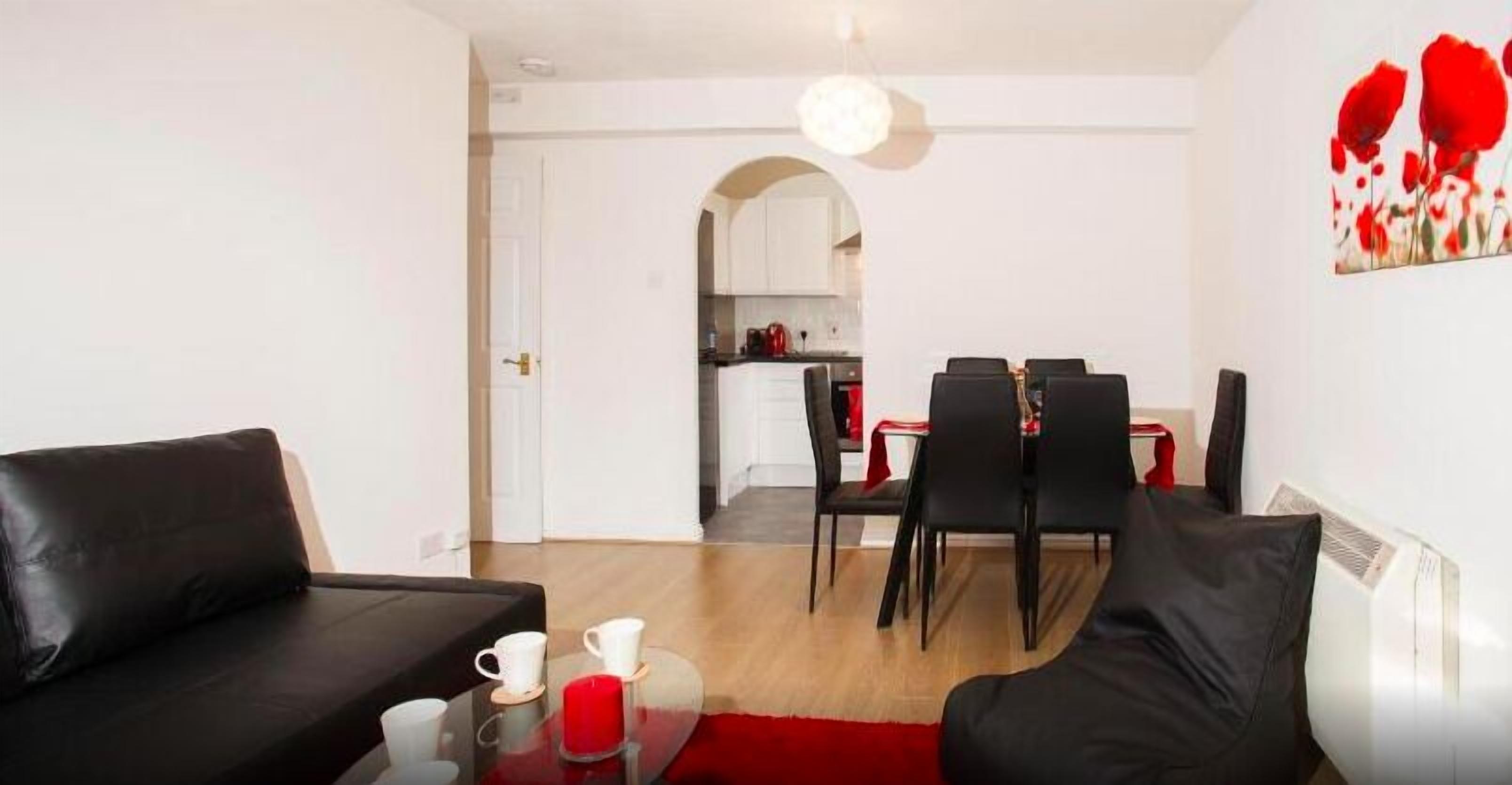 Ein modernes Wohnzimmer mit einem schwarzen Ledersofa, einem Glastisch mit roten Kerzen und einem Essbereich mit roter Tischdecke.