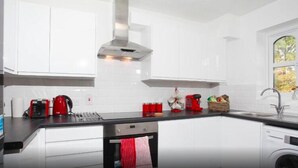 A modern kitchen with white cabinets, a black countertop, a red kettle, and a coffee maker. - Northwick Park Apartment (Harrow)