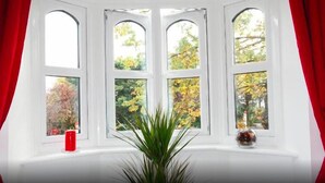 A room with a bay window featuring four panes, a red candle on the sill, and a potted plant in the center. - Northwick Park Apartment (Harrow)