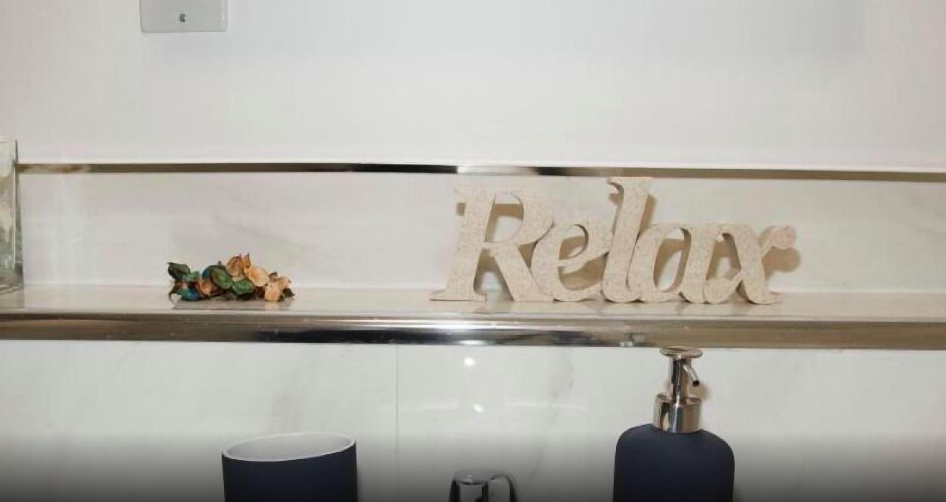 A bathroom with a white sink, a mirror, and a decorative sign with the word "Relax".