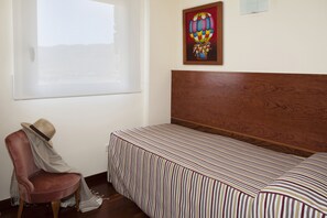 Een slaapkamer met een enkel bed, een stoel, een raam en een schilderij aan de muur.