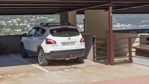 A white car parked in a covered parking area with a view of a hillside and buildings in the background. - TORRE GRAND LUXE APARTMENT (El Port de la Selva)