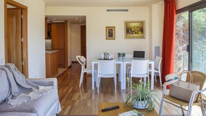 A living room with a sofa, a coffee table with a book and remote, a dining area with chairs and a table, and a kitchen in the background. - TORRE GRAND LUXE APARTMENT (El Port de la Selva)