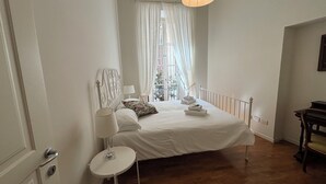 A bedroom with a bed, a bedside table, a lamp, a window with curtains, and a view of the outside. - AD Verona Flat (Verona)