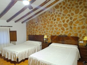 Ein Zimmer mit zwei Betten, einer Steinwand, Holzbalken und einem Deckenventilator.