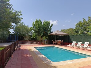 Ein rechteckiger Pool mit Fliesenrand, umgeben von einem Holenzaun und einem gepflasterten Weg.