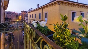 A balcony with a wrought iron railing, potted plants, and a view of a street with buildings. - Arela (Verona)