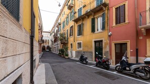 A narrow street lined with colorful buildings, parked scooters, and a clear view of the street. - Arela (Verona)