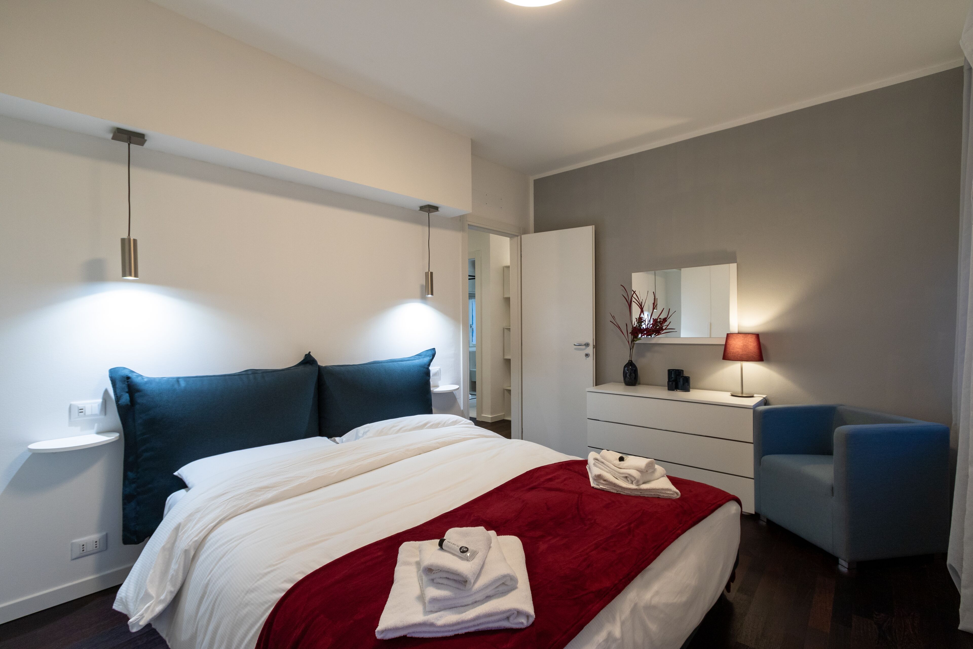 Una habitación de hotel moderna con una cama bien hecha, una mesita de noche con lámpara, una silla y un aparador.