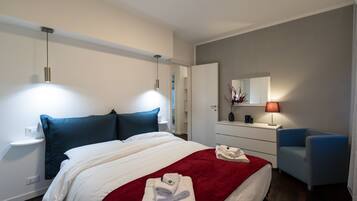 Una habitación de hotel moderna con una cama bien hecha, una mesita de noche con lámpara, una silla y un aparador.