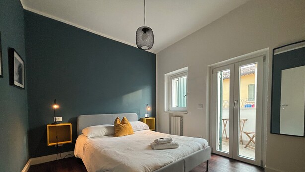 A bedroom with a bed, bedside lamps, a window, and a door leading to a balcony. - Arela (Verona)