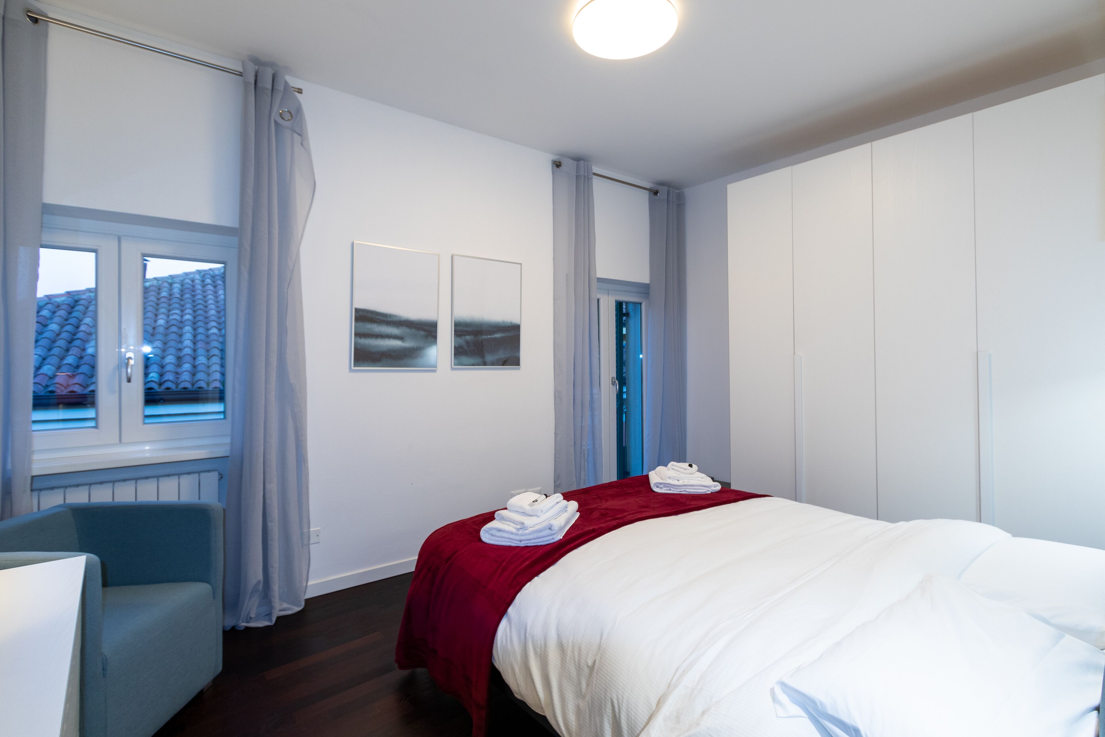 A hotel room with a bed, a chair, a window with curtains, and a door.