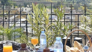 A table set with Moroccan breakfast items, including bread, pastries, and orange juice, overlooking a cityscape with a castle on a hill. - Riad Fes Madaw (Fes)