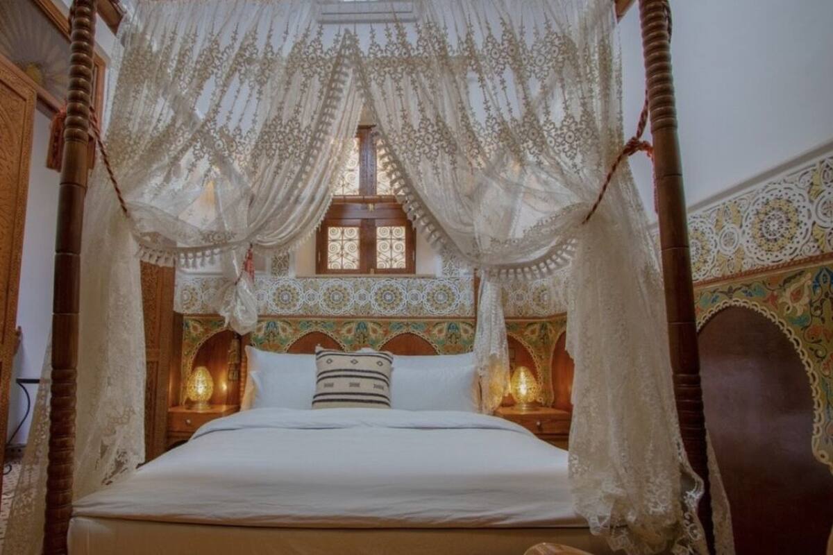 A four-poster bed with a canopy, ornate wooden headboard, and patterned wall decor.