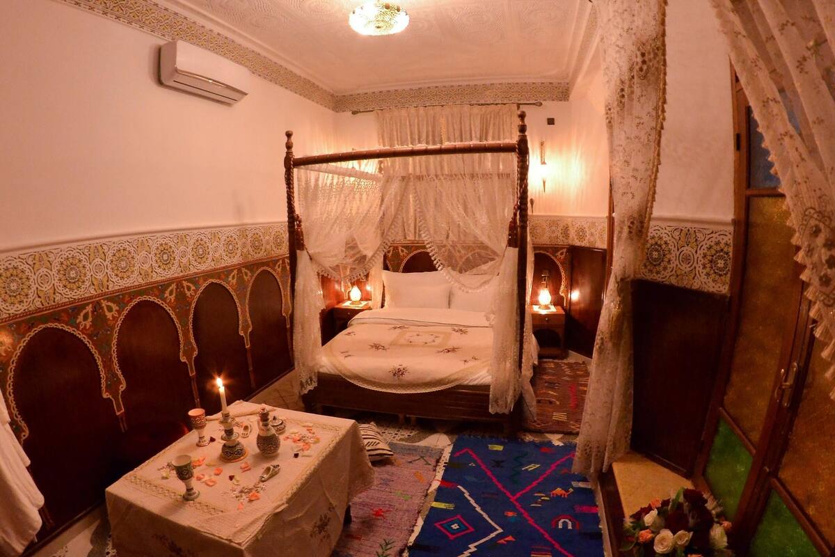 A traditional room with a four-poster bed, a small table with candles, and a patterned rug.