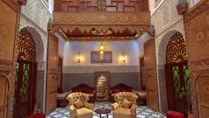 An ornate interior with intricate tile work, two plush armchairs, a small table, and a mirror. - Riad Fes Madaw (Fes)