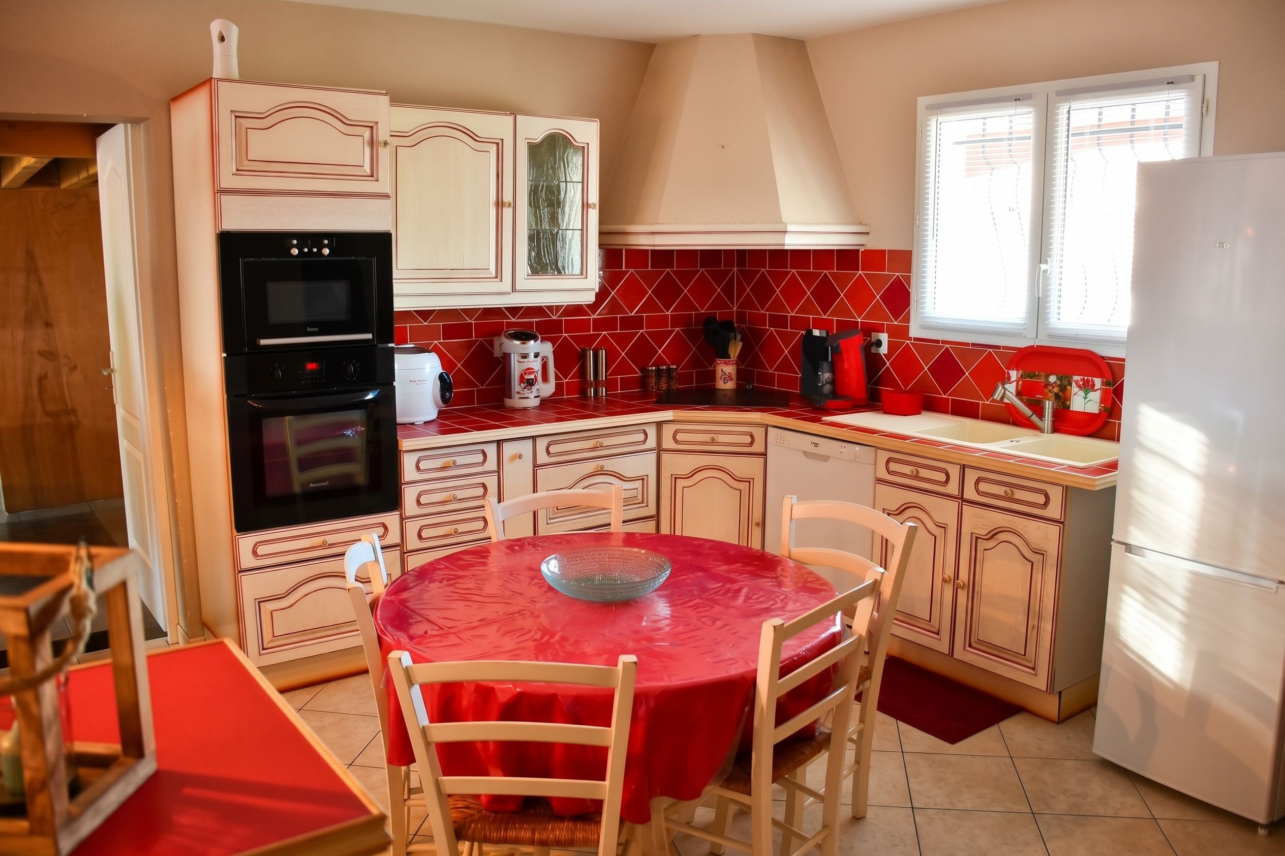 A compact kitchen with a dining area, featuring a red tiled backsplash, a built-in oven, and a refrigerator.