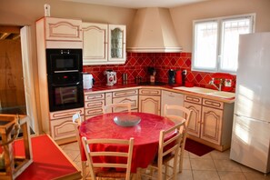 A compact kitchen with a dining area, featuring a red tiled backsplash, a built-in oven, and a refrigerator. - Homerez - Villa in Carcassonne (Carcassonne)