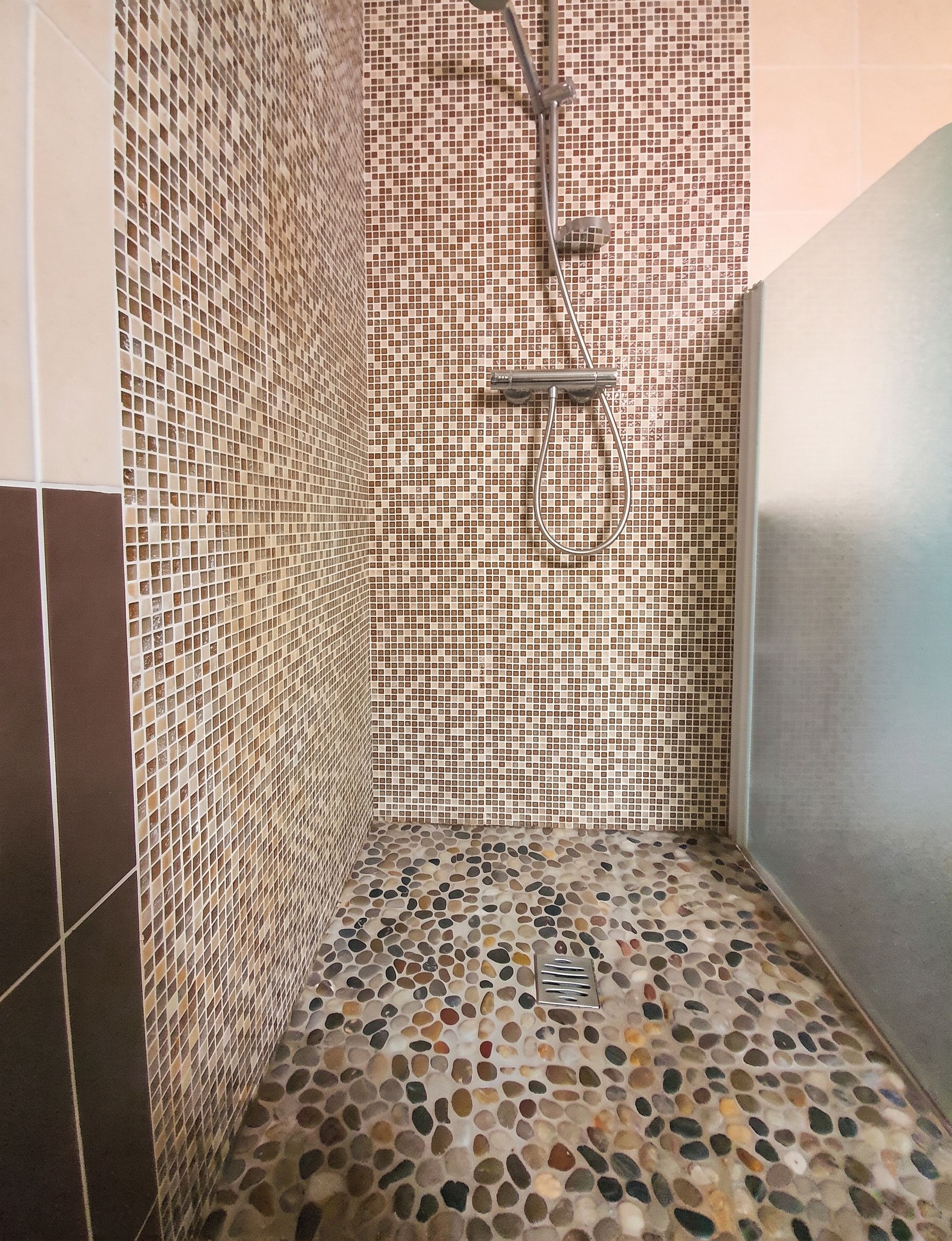 Ein Duschbereich mit Mosaikfliesen an den Wänden und einem Boden mit Kieselmuster.