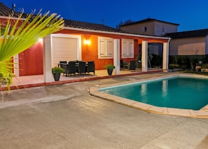 A residential property with a swimming pool, outdoor seating, and a covered patio area.