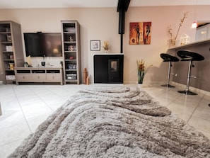A modern living room with a flat-screen TV, a fireplace, a dining area with bar stools, and a large shaggy rug. - Homerez - Villa in Carcassonne (Carcassonne)