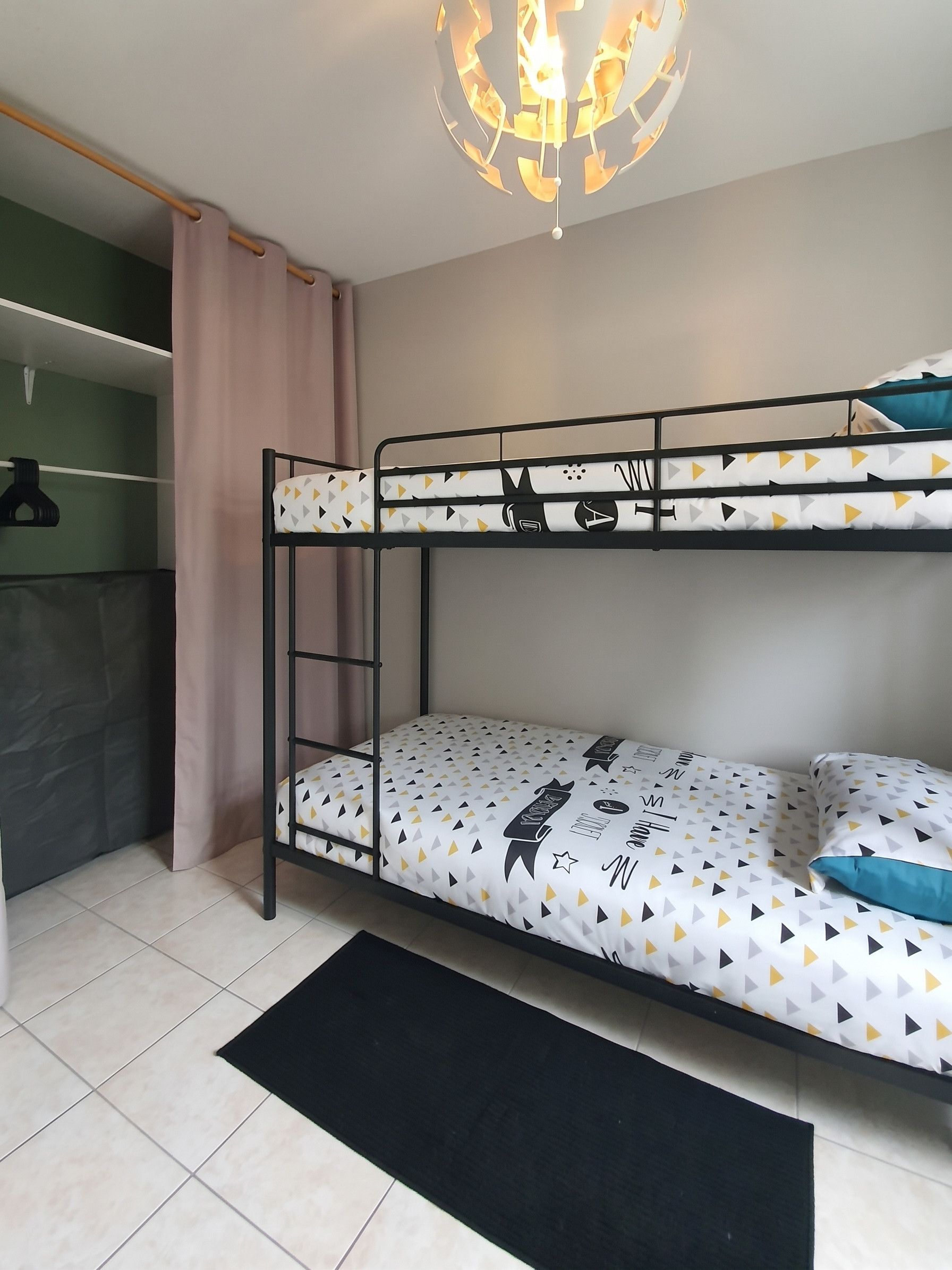 Un lit superposé avec une couvre-lit à motifs géométriques, un tapis de sol noir et un luminaire suspendu.