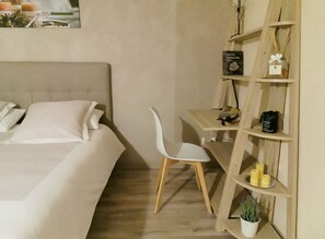 A bedroom with a bed, a white chair, a wooden shelf with various items, and a small potted plant. - Homerez - Villa in Carcassonne (Carcassonne)