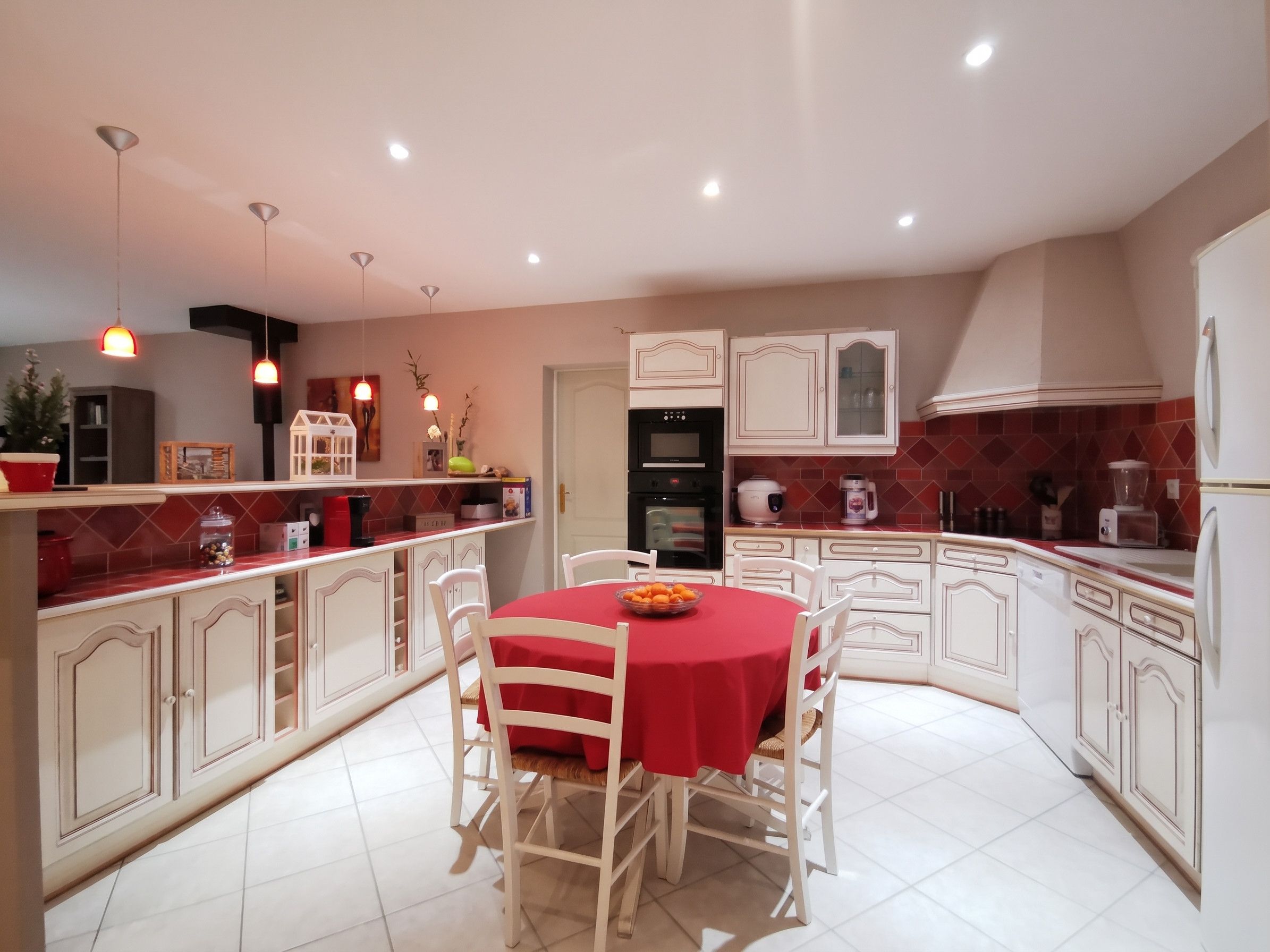 Une cuisine moderne avec des meubles blancs, une table à manger rouge et des luminaires suspendus.