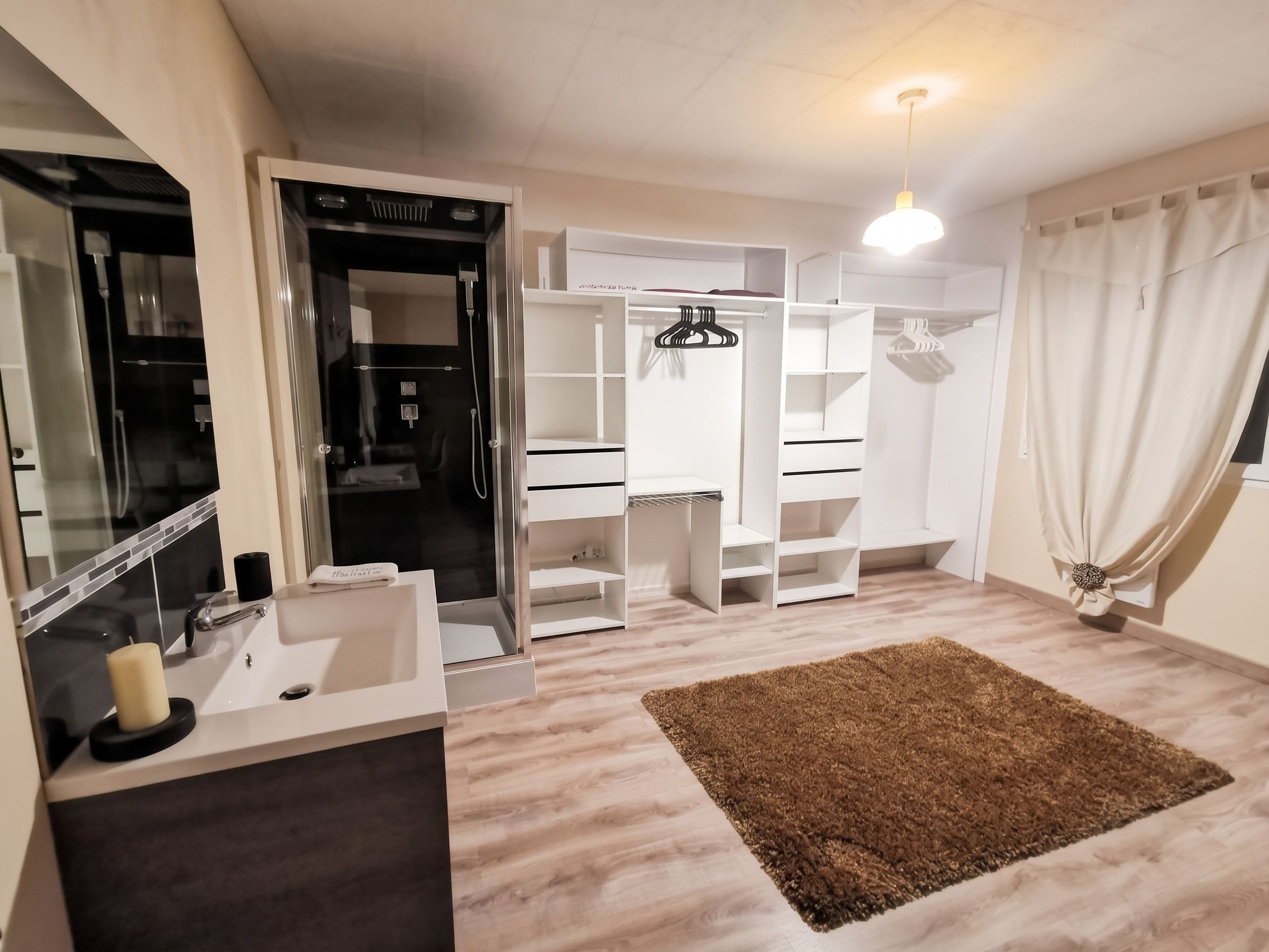 Een moderne badkamer met een wastafel, spiegel, douche en kleedkamer met planken en een kledingroede.