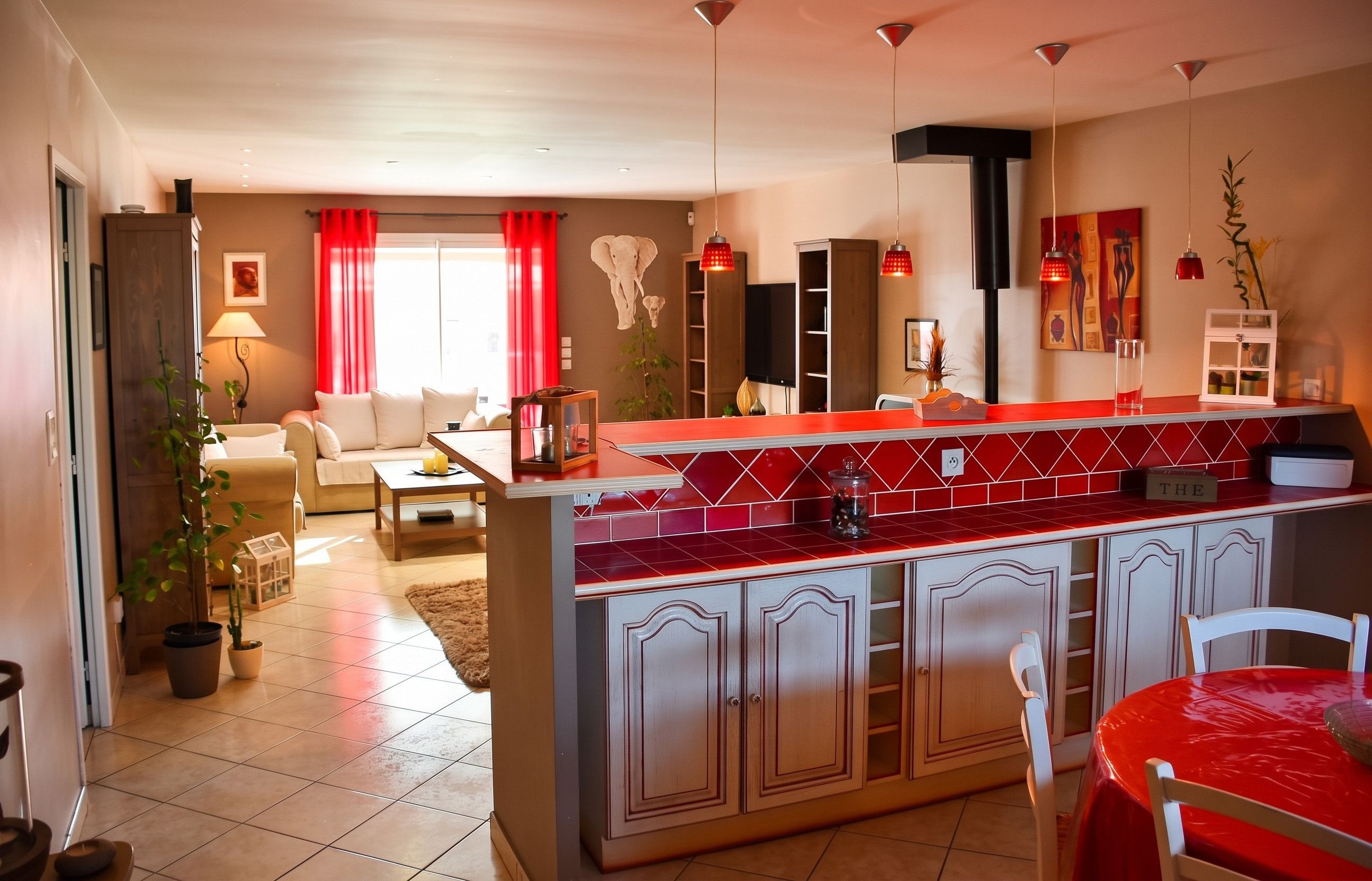 Une cuisine moderne avec un plan de travail rouge, des armoires blanches et un coin repas comprenant une table et des chaises rouges.